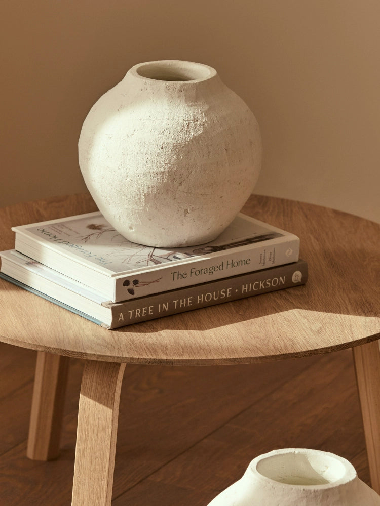 Boho style white ceramic vases displayed on stack of books on a wooden table.